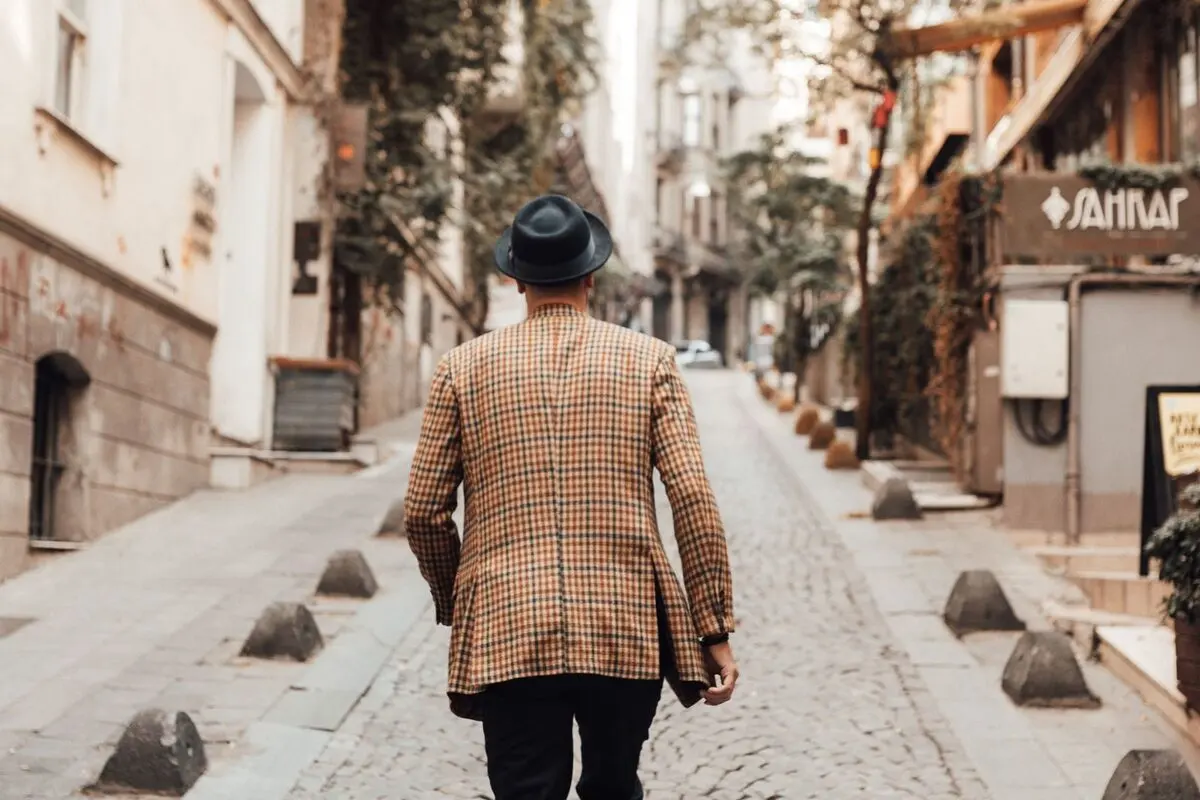 A man in a hat walking down a cobblestone street